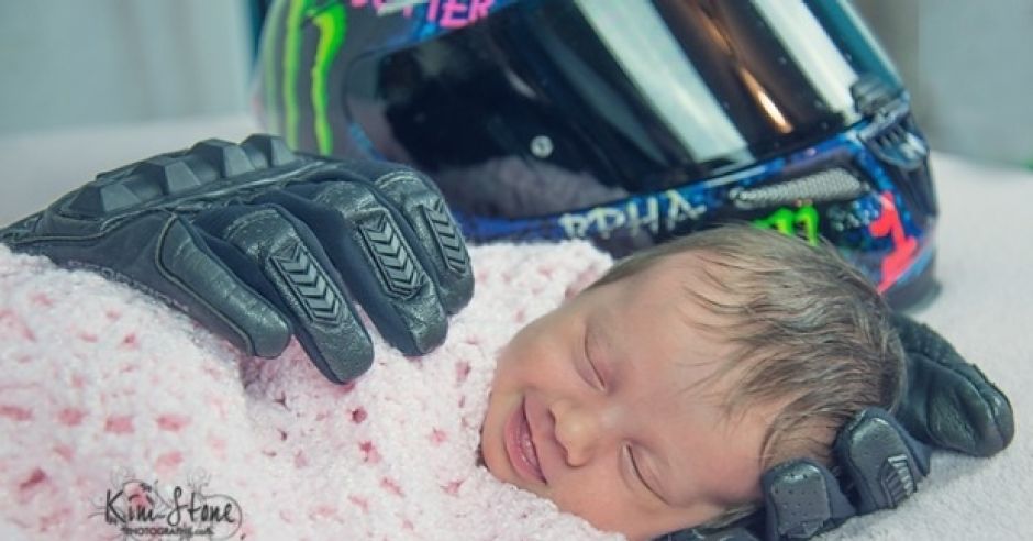 Dziewczynka uśmiecha się leżąc w rękawicach motocyklowych taty