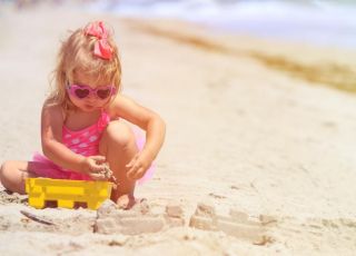 Dziewczynka w okularach przeciwsłonecznych bawi się sama na plaży