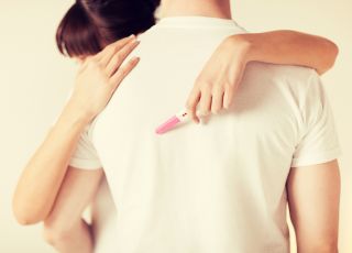 Kobieta przytula mężczyznę trzmając w ręku test ciążowy.