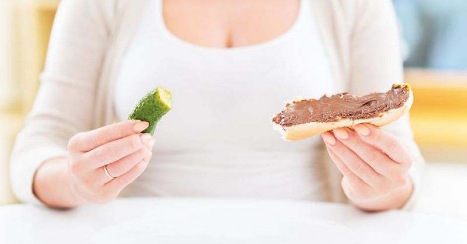 Kobieta w ciąży je kanapkę z Nutellą i ogórka