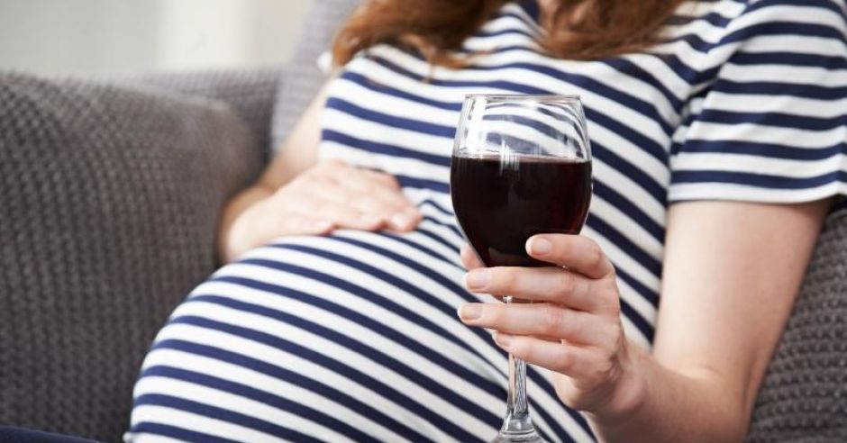 Kobieta w ciąży siedzi na kanapie z kieliszkiem wina