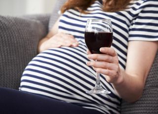 Kobieta w ciąży siedzi na kanapie z kieliszkiem wina