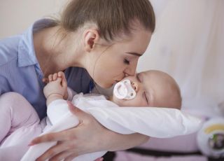 Młoda mama całuje niemowlę w policzek