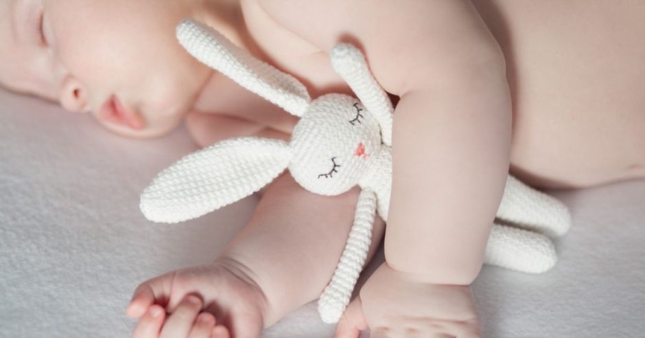 Niemowlę śpi w łóżeczku, przytulając pluszowego króliczka