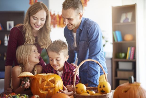 rodzice z dziećmi wspólnie wycinają wzory na dyni w halloween