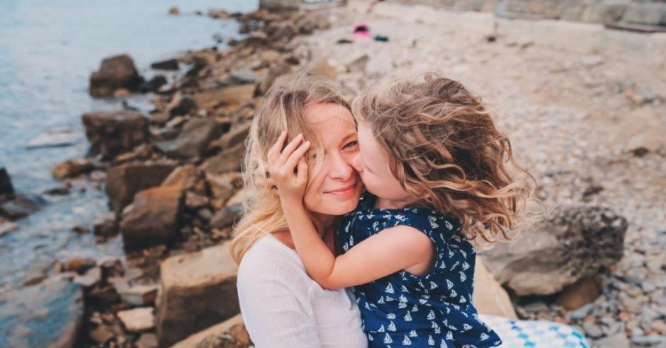 Uśmiechnięta mama przytula na plaży córeczkę